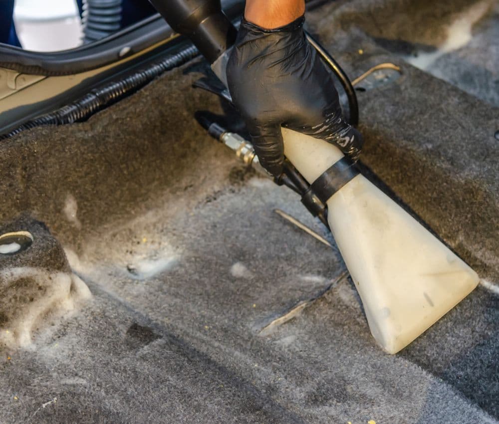 Professional vacuuming a vehicle interior carpet